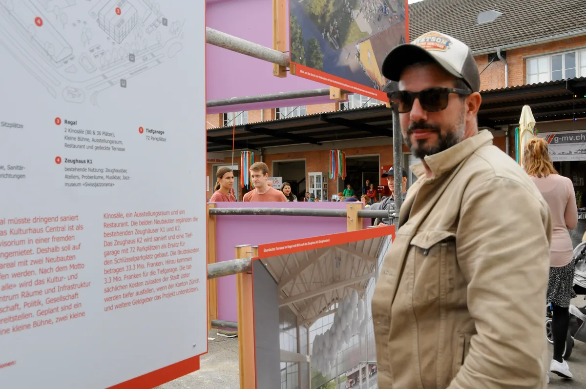 Man sieht einen Festbesucher mit Sonnenbrille vor einer Info-Tafel.